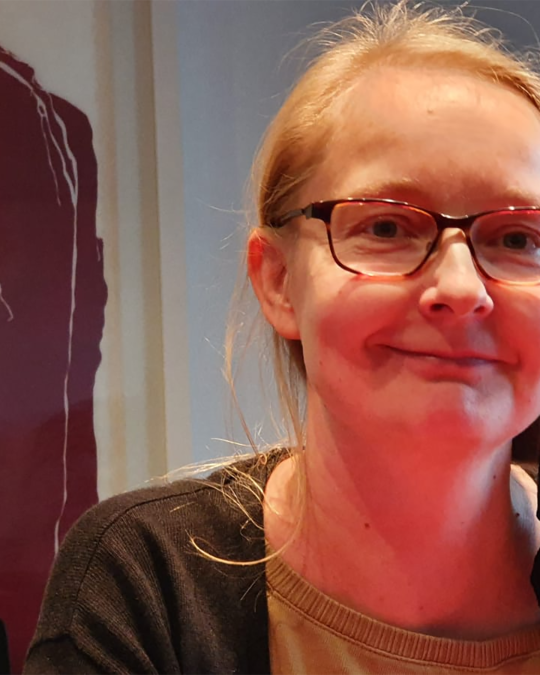 Silmälasipäinen ja vaaleatukkainen Minna hymyilee kameralle.
